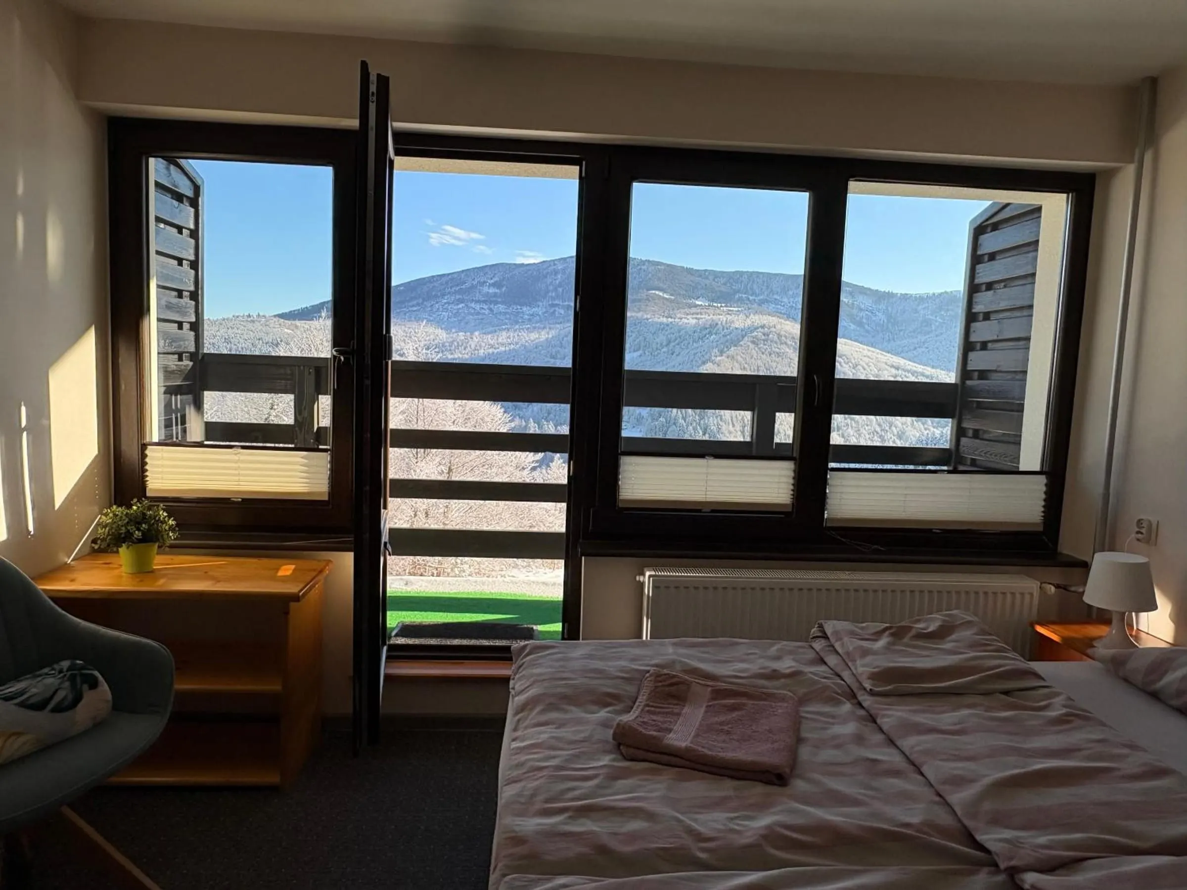 Pokój z dwoma zsuniętymi łóżkami i otwartymi drzwiami na balkon, za oknem zaśnieżone góry